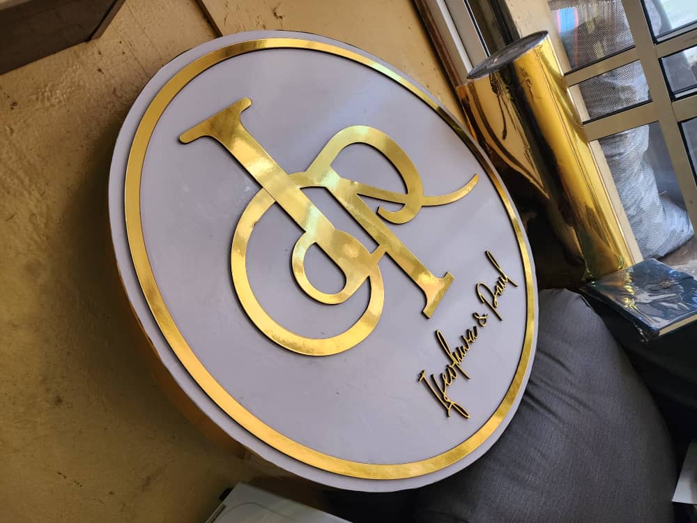 Polished gold IP monogram on round white acrylic wedding signage with cursive names