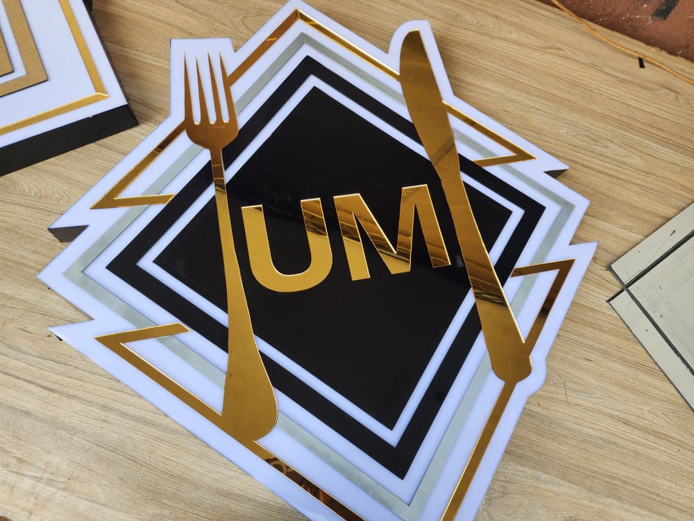 Layered acrylic UM Kitchen logo with mirror-gold fork, knife and monogram