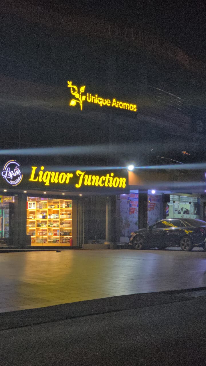 Illuminated yellow Liquor Junction storefront sign at night with Unique Aromas above